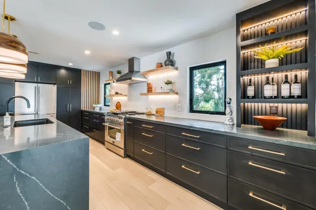 Kitchen with dark cabinets, a waterfall island and lit open shelves