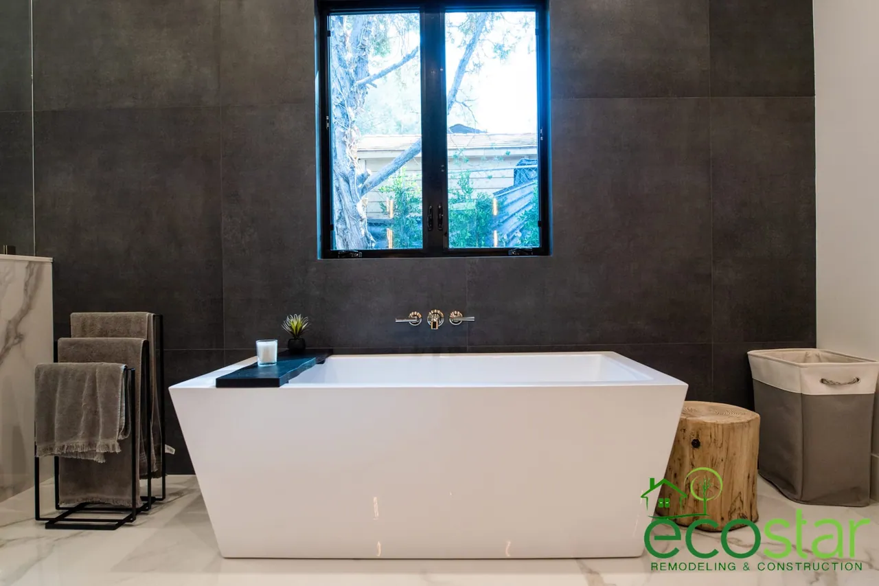 Freestanding tub under an operable window, with large-format wall tile and a marble-look tile floor, in a bathroom remodeled by EcoStar Remodeling & Construction