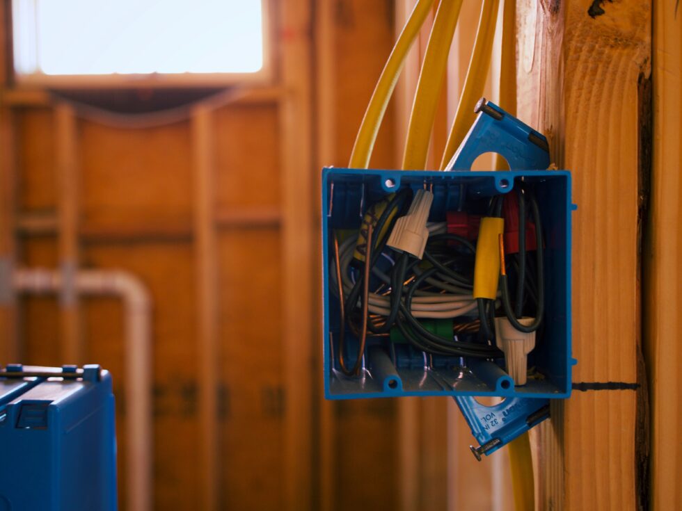 New electrical wiring run into a blue box inside an open wood stud wall